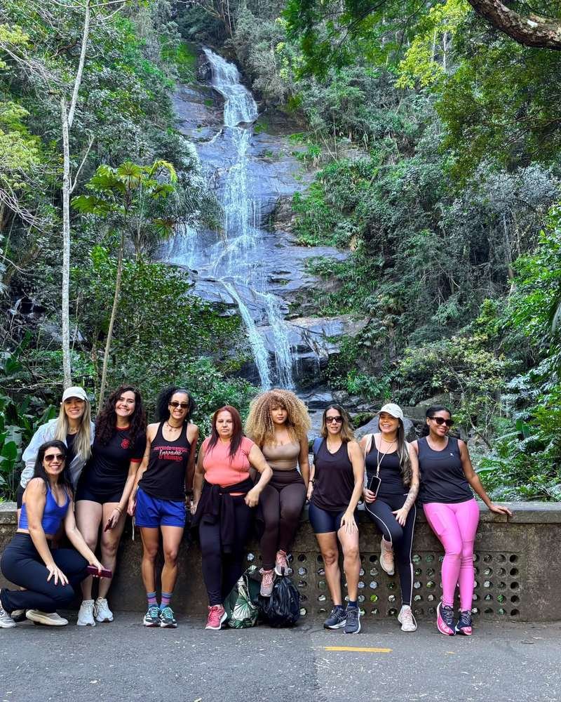 Dez participantes em roupa de treino, lado a lado em frente a uma cachoeira cercada de mata fechada.
